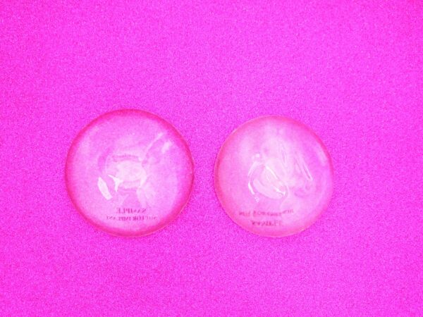 One pair of breast implants (prostheses) flat laid on bright pink background