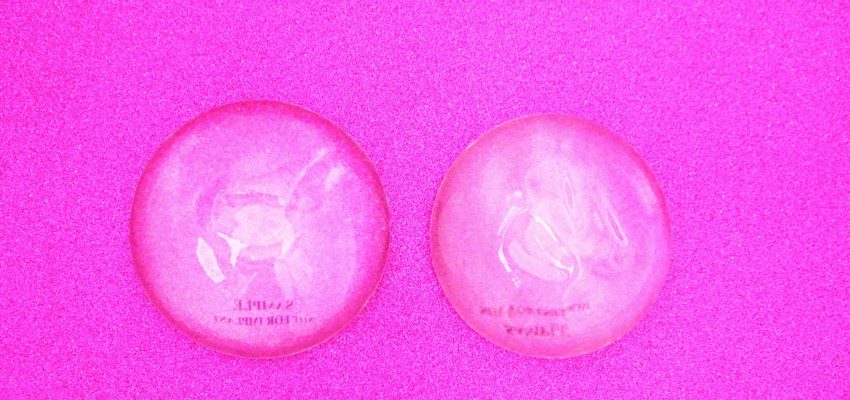 One pair of breast implants (prostheses) flat laid on bright pink background