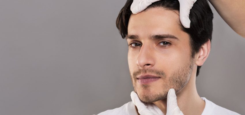 Plastic surgeon examining male patient face, empty space